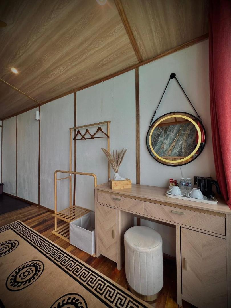 A modern bedroom at Seaweed Village near the Tun Sakaran Marine Park offering a vanity desk, an illuminated mirror, clothes rack, rustic timber floor boards, and air conditioning.