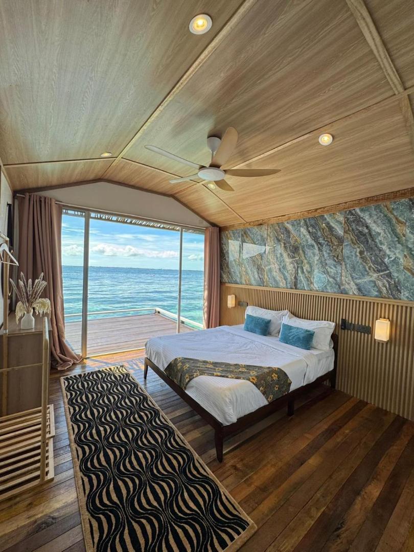 A stunning bedroom at Seaweed Village near Bum Bum Island showing a large bed facing floor to ceiling glass doors with seaviews, a unique marble feature wall, authentic hardwood floors, and AC.